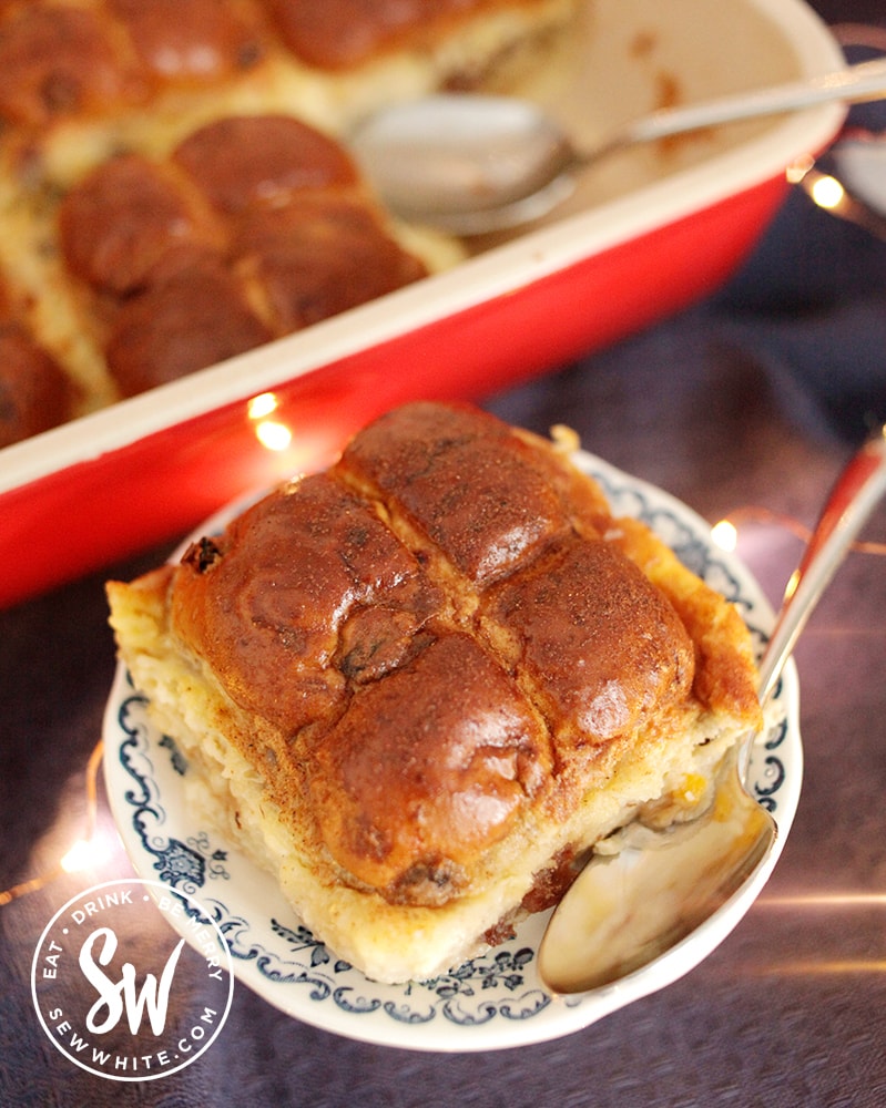 Oven baked Hot Cross Bun Dessert cooked in a red Le Creuset oven proof dish. Hot cross bun bread and butter pudding slice on a little plate