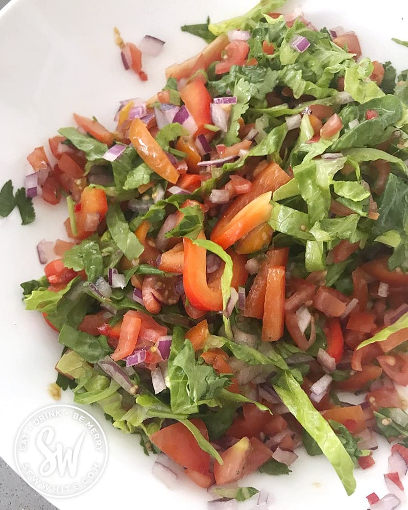 A white bowl with a mix of tomatoes, lettuce, pepper, cilantro, red onion and chilli