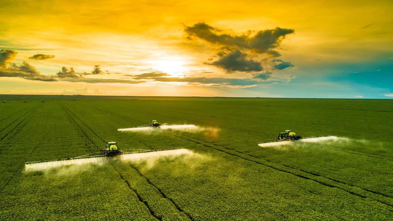 três máquinas agrícolas realizando pulverização em uma lavoura de soja com destaque para o horizonte e pôr do sol. Agricultura digital e planejamento safra