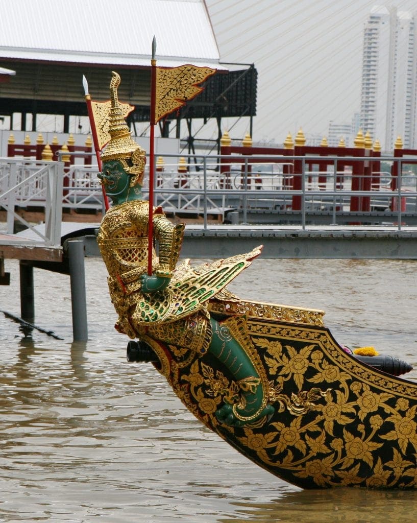 Green faced Thai mythical creature on bow of boat sitting near dock.