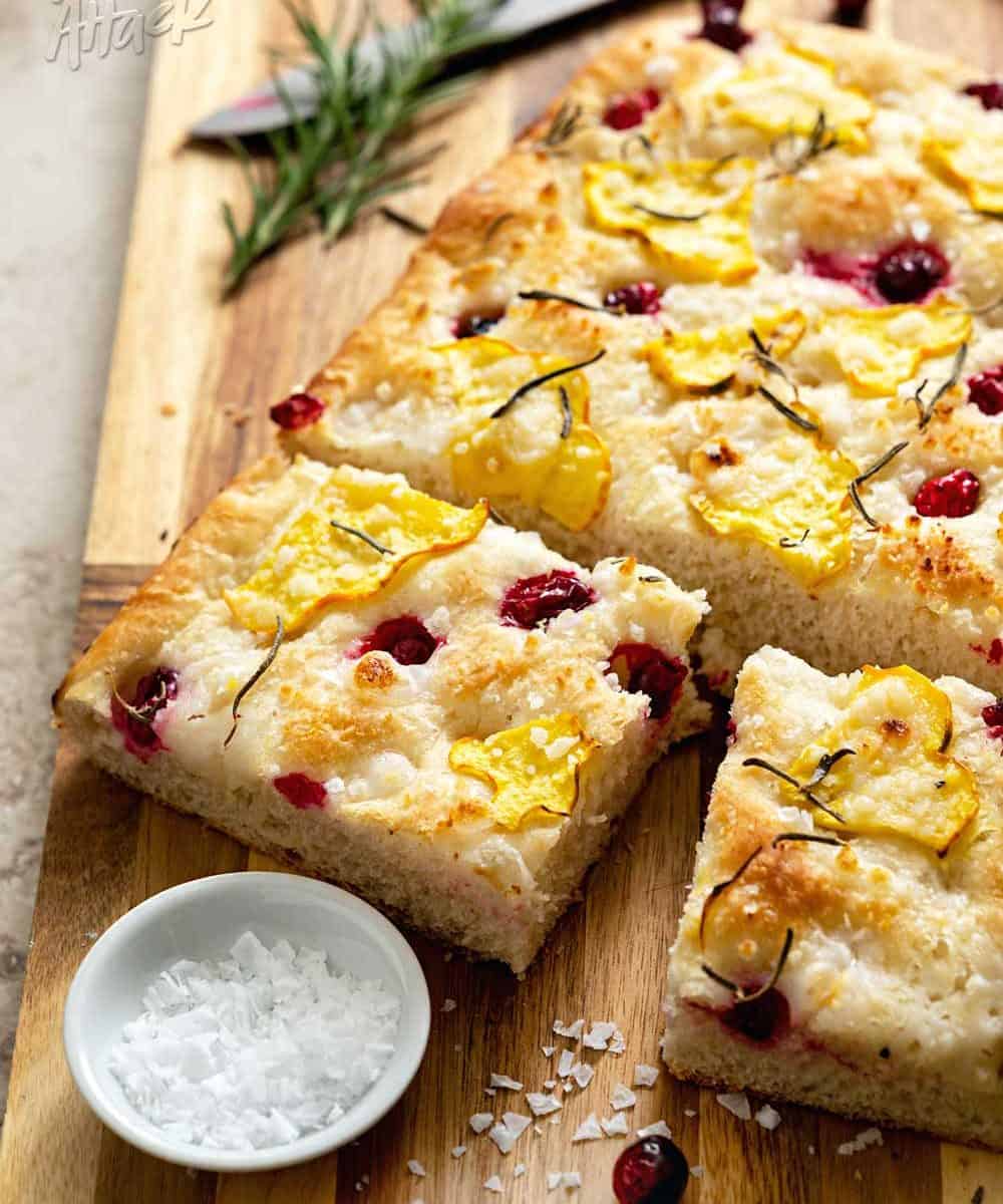 Focaccia topped with squash and cranberries on a wood cutting board