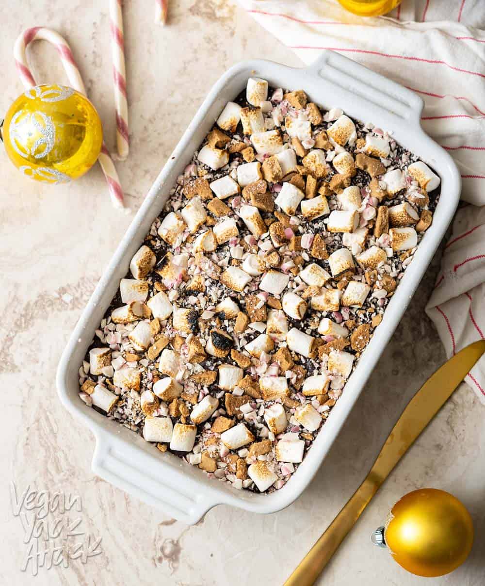 Whole baking dish of peppermint s'mores fudge with a linen, Christmas ornaments, and gold knife