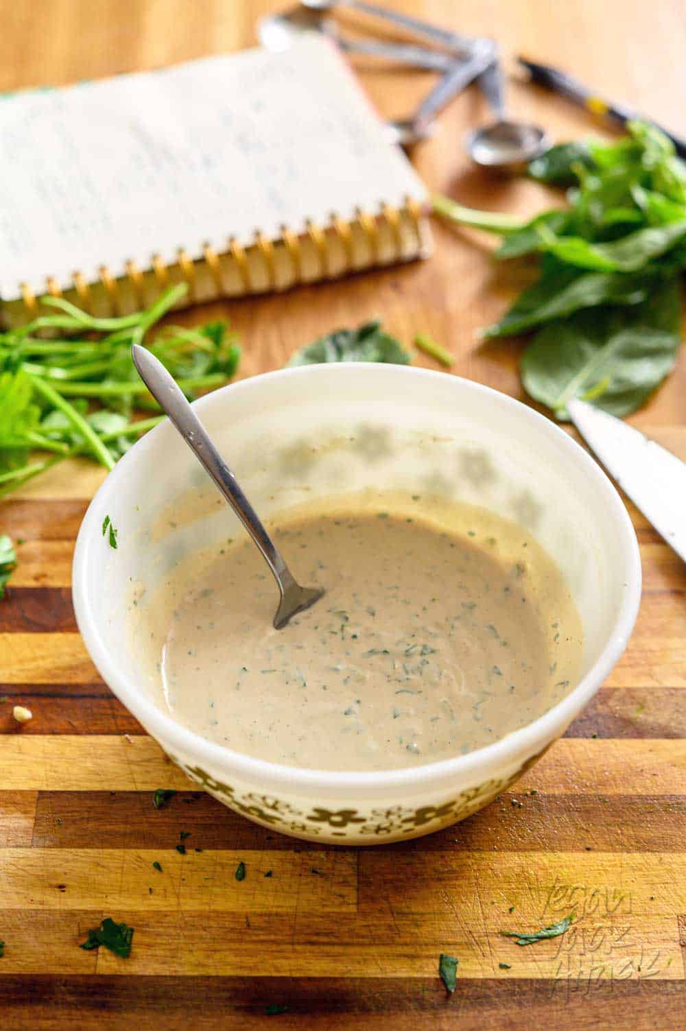 Image of mixing bowl filled with herbed tahini sauce on a cutting board