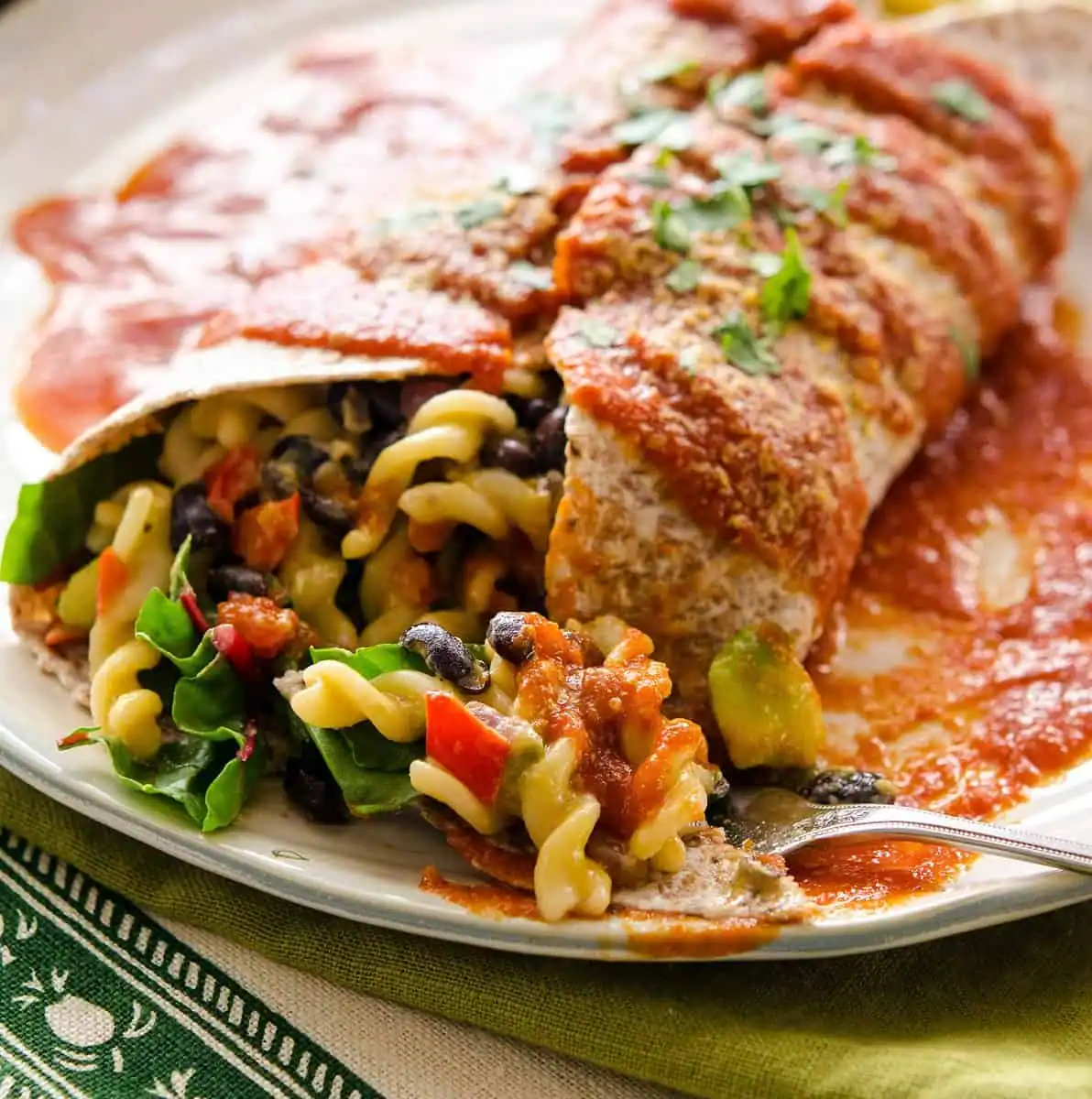 A large burrito stuffed with Mac and cheese and topped with red sauce