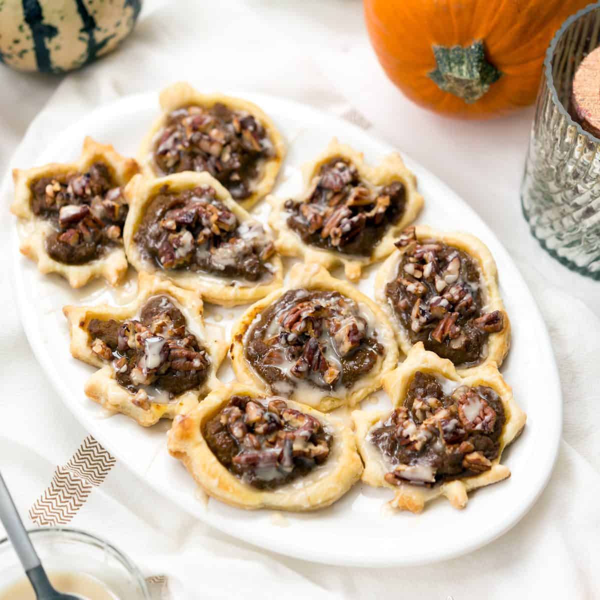 A white, oval platter filled with leaf-shaped pumpkin pastries topped with glaze
