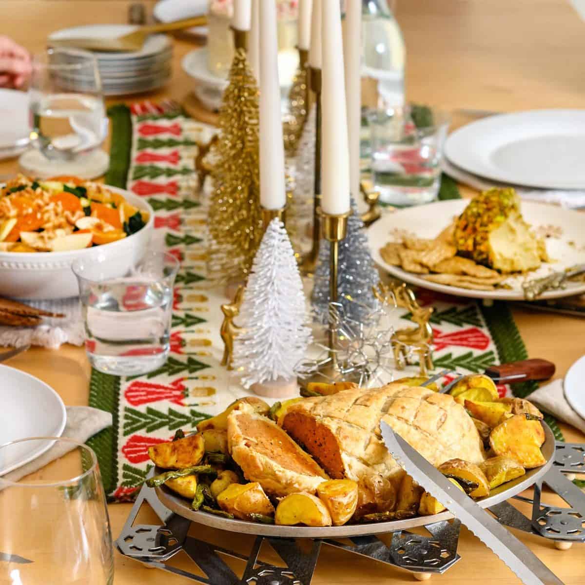Image of an ultimate vegan holiday dinner spread with table runner and dishes, including salad and sliced seitan Wellington