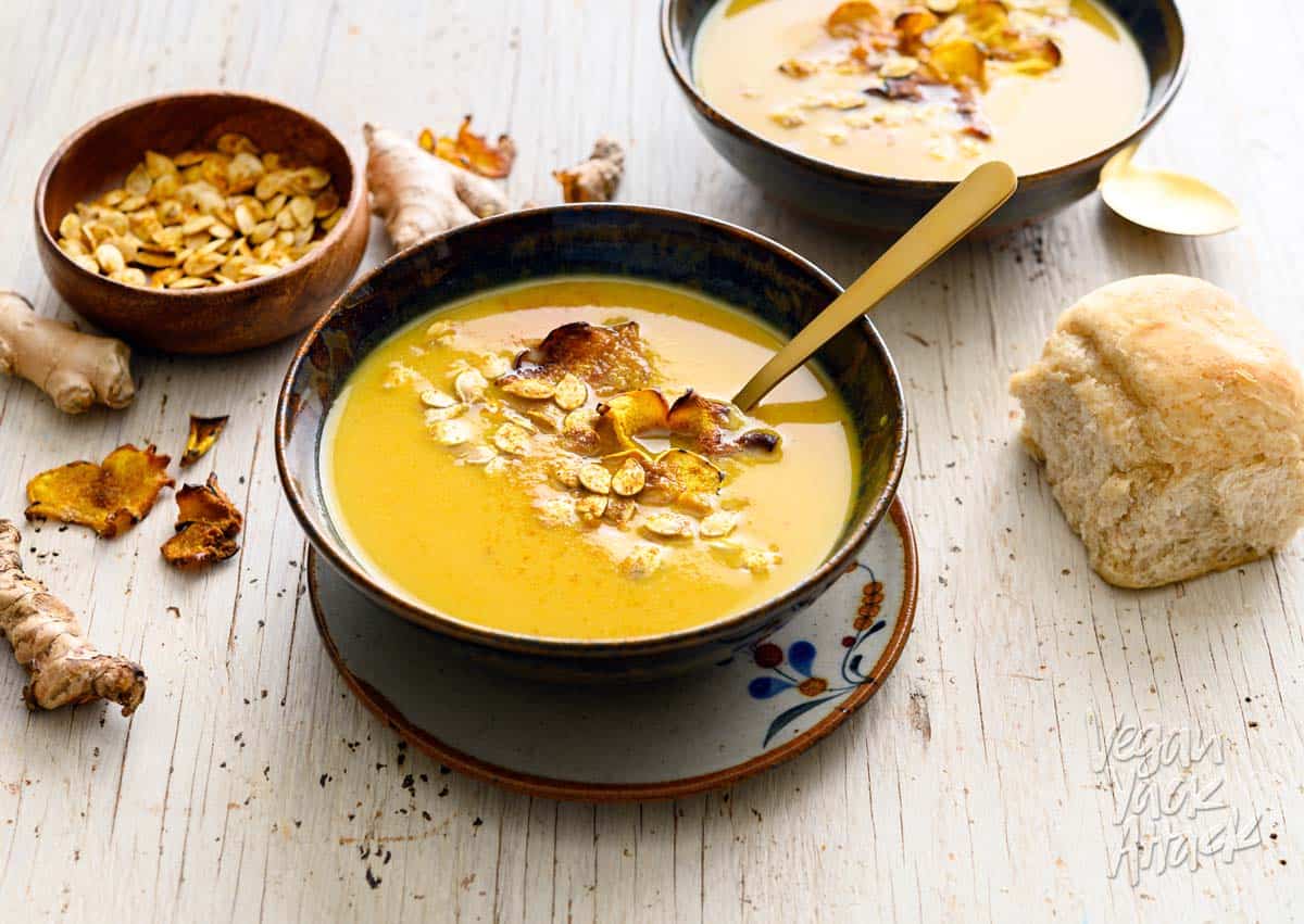 Two bowls of ginger turmeric squash soup with toasted seeds and a bread roll
