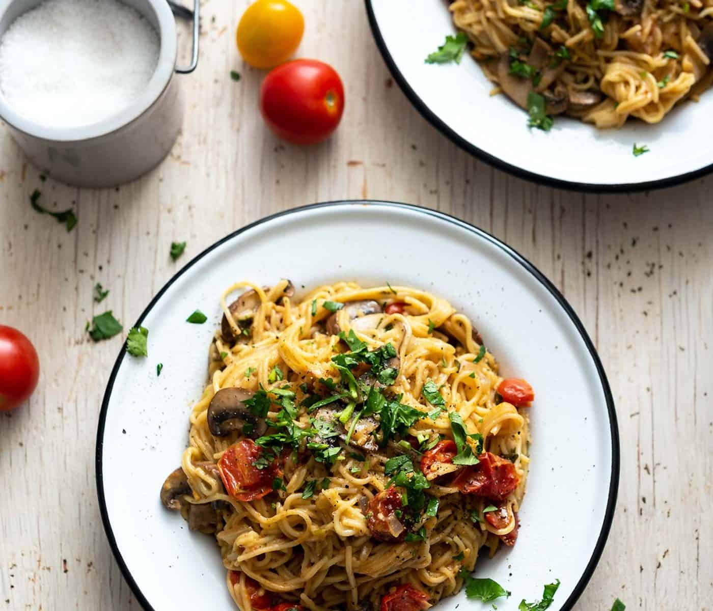 Image of two bowls of pasta on a white wood table top, with salt on the side