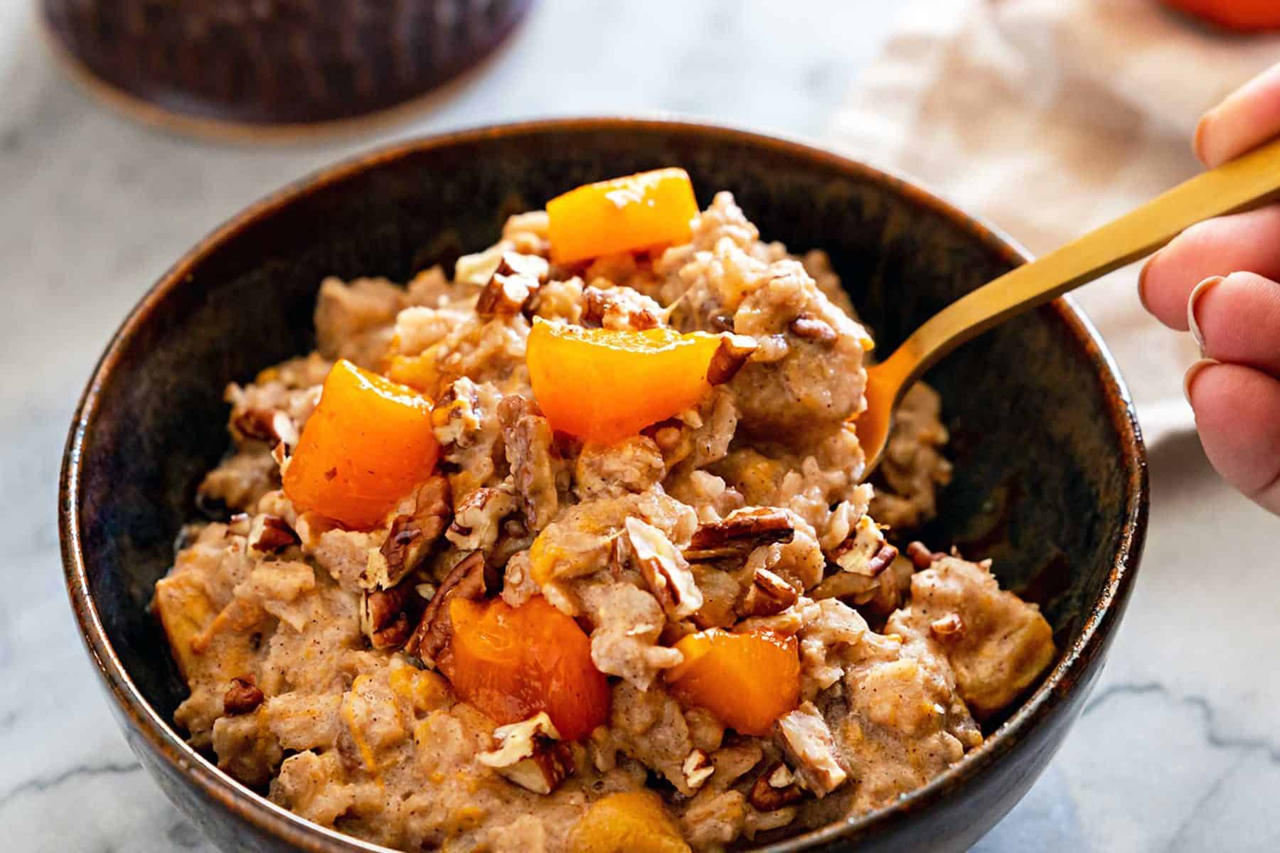 Ceramic bowl filled with persimmon oatmeal, and golden spoon, with a cup of coffee
