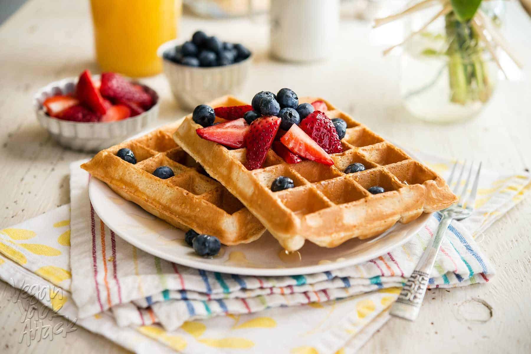 two berry pineapple belgian waffles on a white plate, topped with berries, sitting atop two colorful napkins