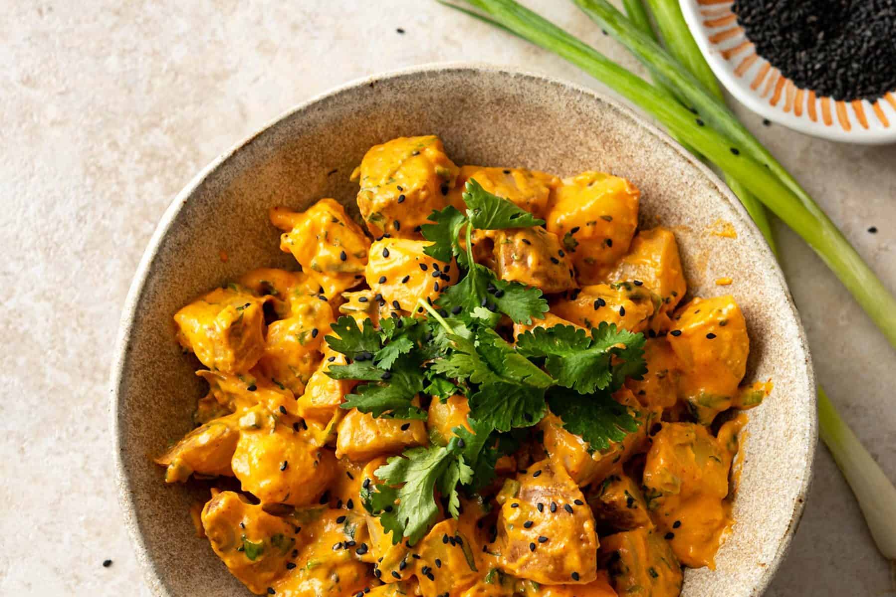 Large ceramic bowl filled with sriracha potato salad that is topped with sesame seeds and cilantro