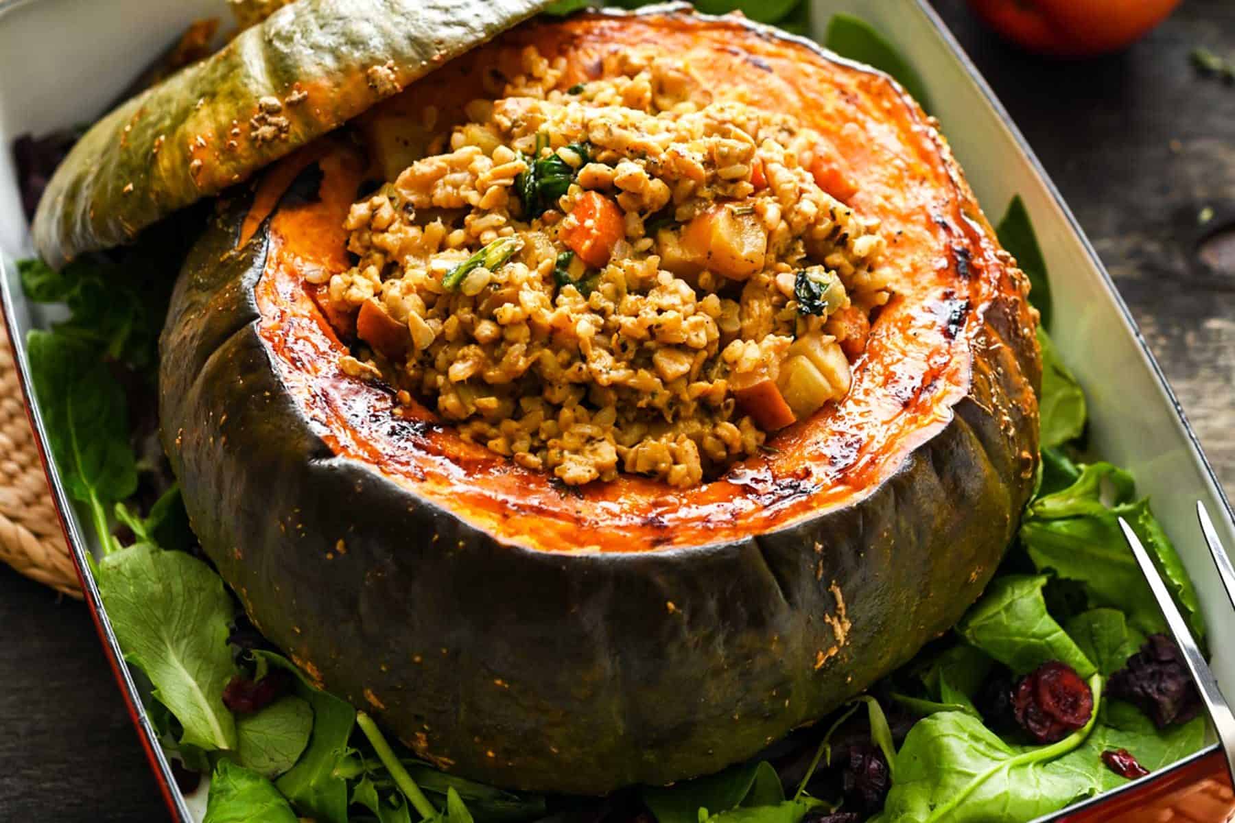 A large, roasted kabocha squash centerpiece, in a casserole dish, stuffed with a rice/tempeh mixture, on a dark background.