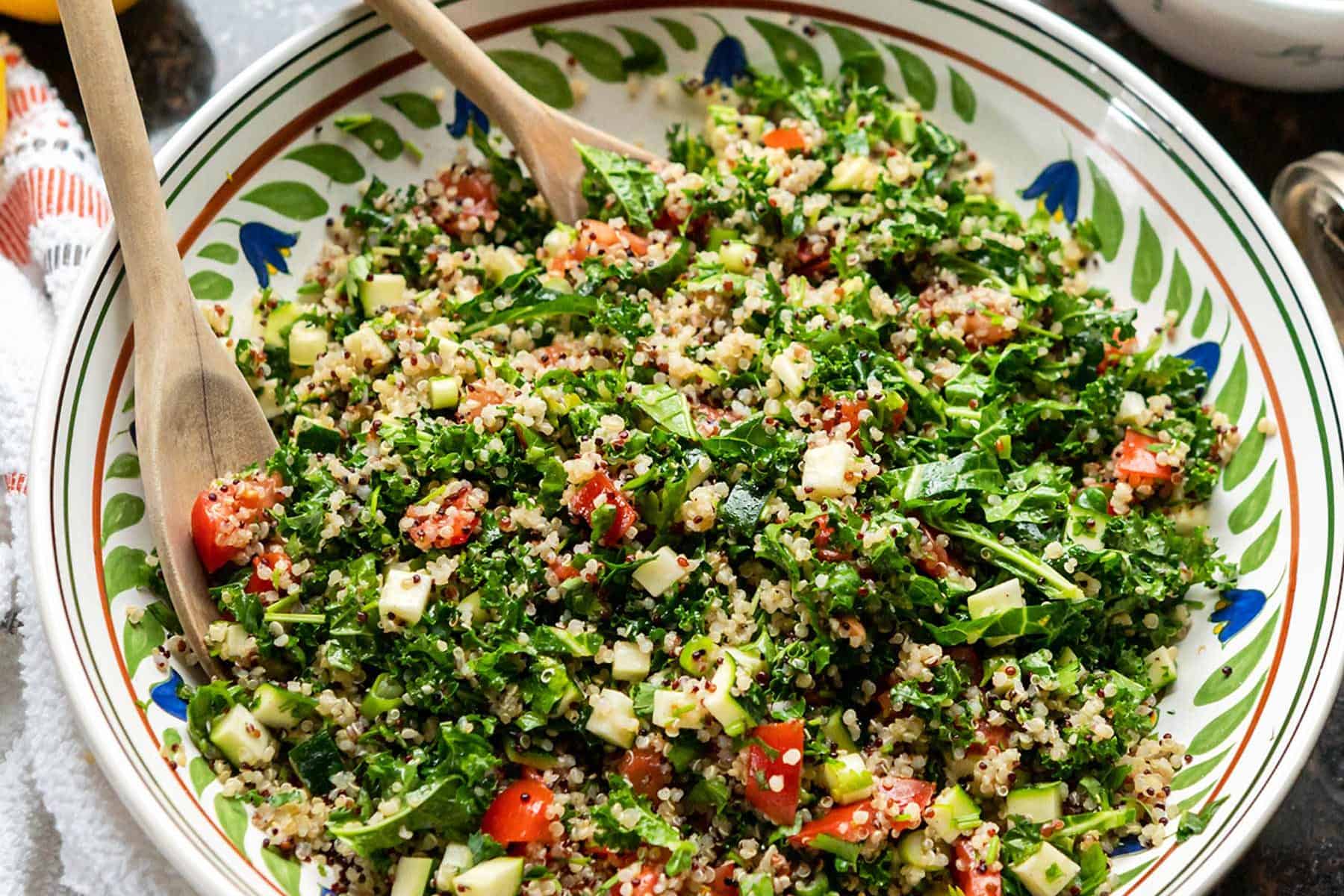 Image of kale quinoa tabbouleh salad in a large ceramic bowl, on granite countertop.