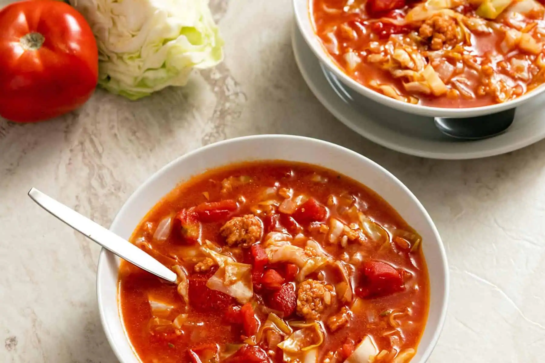Two bowls of cabbage roll soup on a marble background