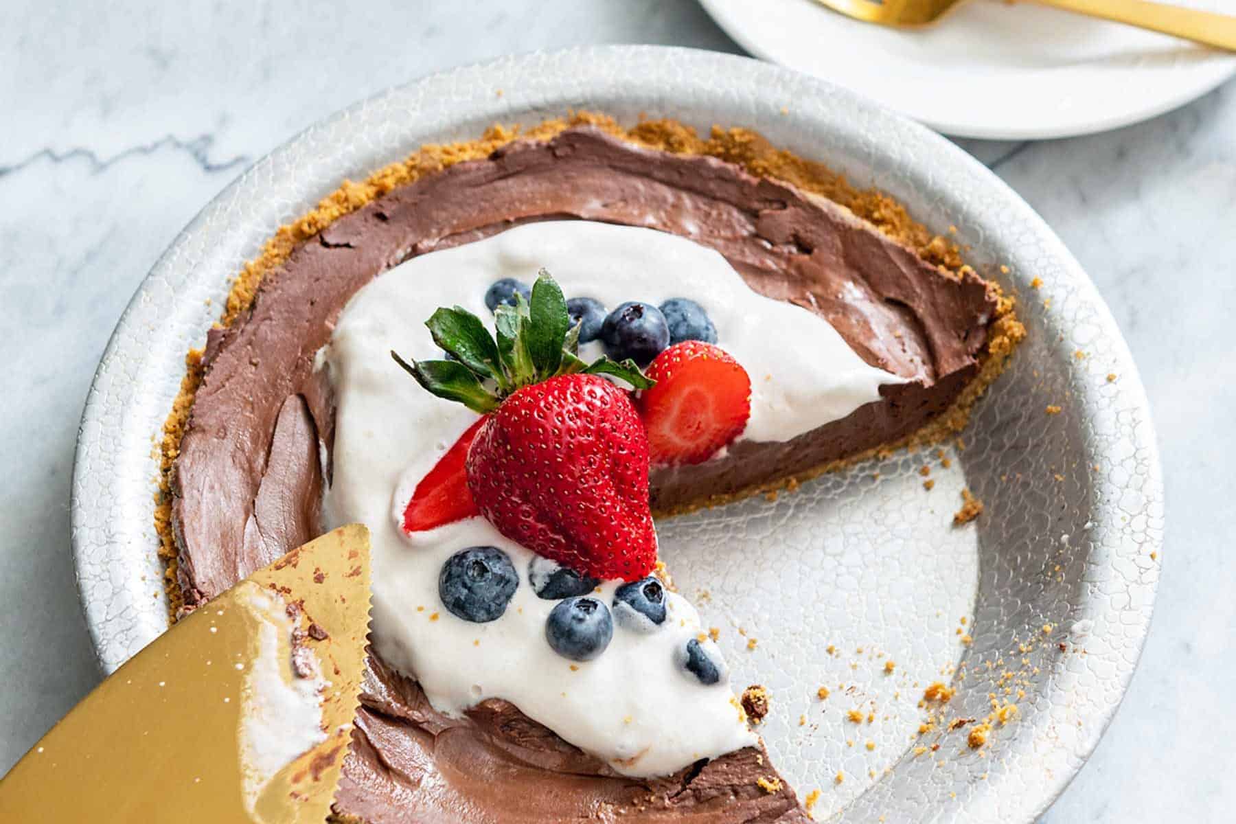 Slice of chocolate pie on a plate next to whole pie and gold pie server