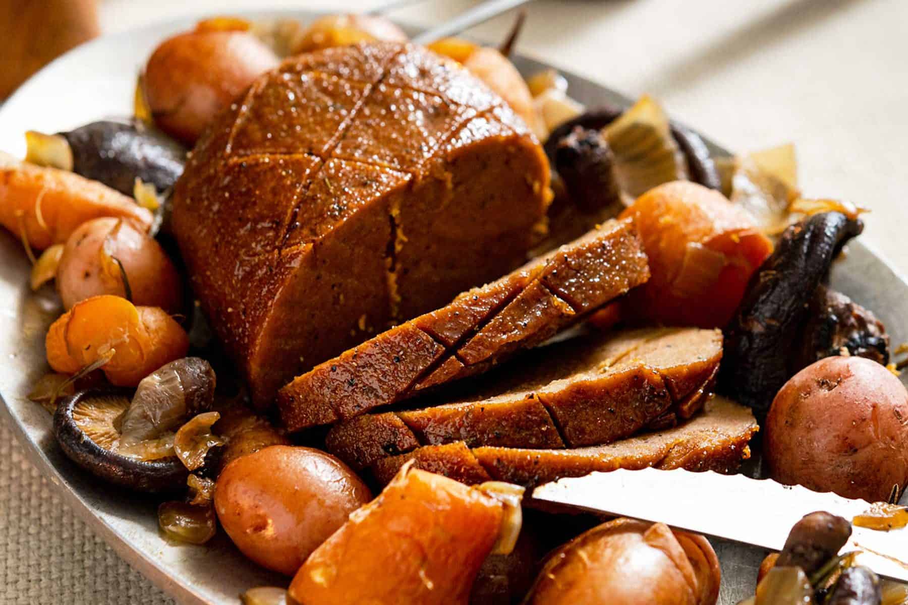 Sliced seitan roast on a metal platter with cooked vegetables