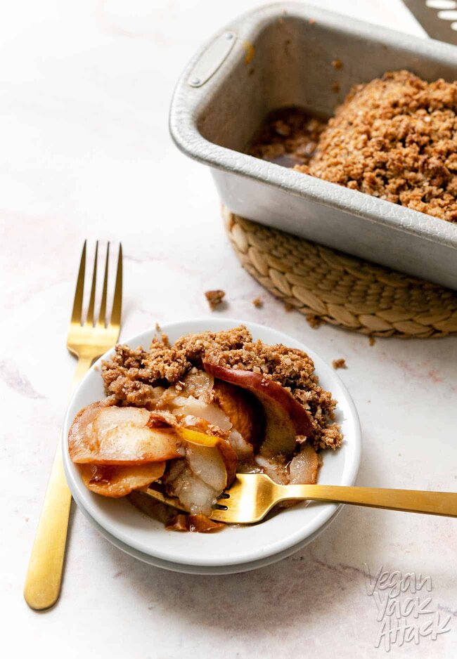 A small plate with a scoop of apple pear crisp with gold forks