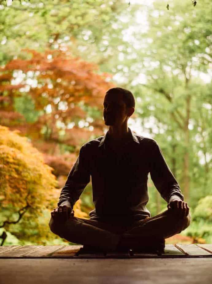 Trainer alleen zittend in meditatiehouding met natuur op de achtergrond: Volg een individuele mindfulnesstraining.