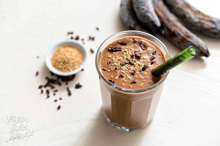 One large glass filled with chocolate sesame smoothie, with seeds, nibs, and bananas on the side
