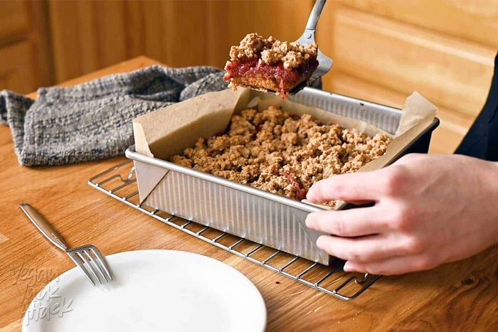 Spatula lifting a piece of strawberry crumble bar out of a baking pan
