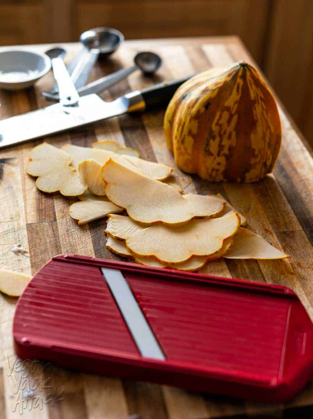 Thinly sliced acorn squash next to a red mandolin