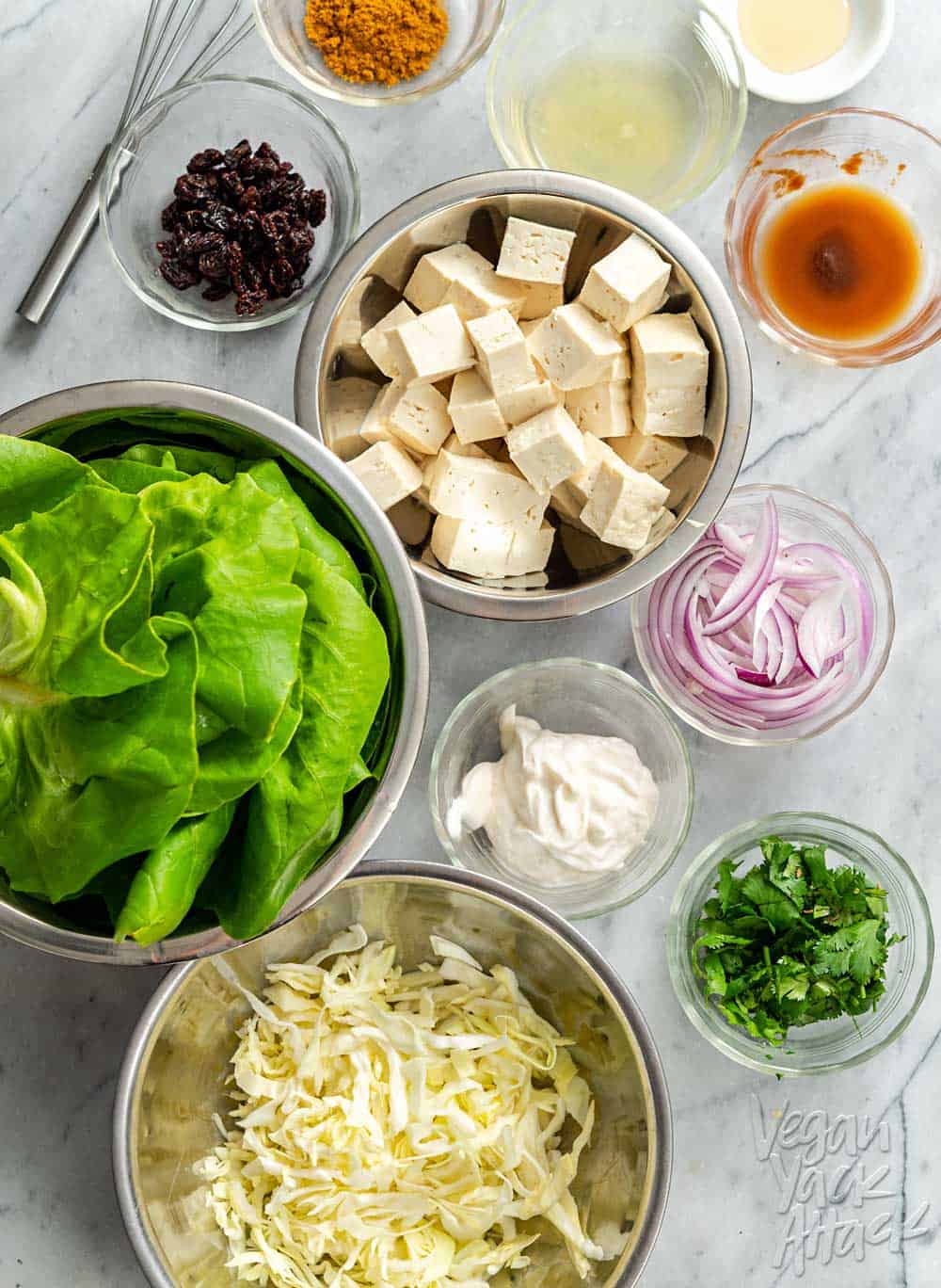 Ingredients for lettuce cups in steels bowls: tofu, cabbage, red onion, raisins, cilantro, vegan mayo, etc.