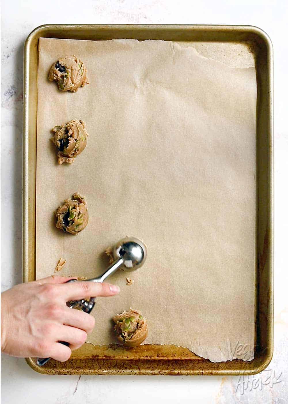 Scooping vegan cookie dough onto a parchment-lined baking sheet