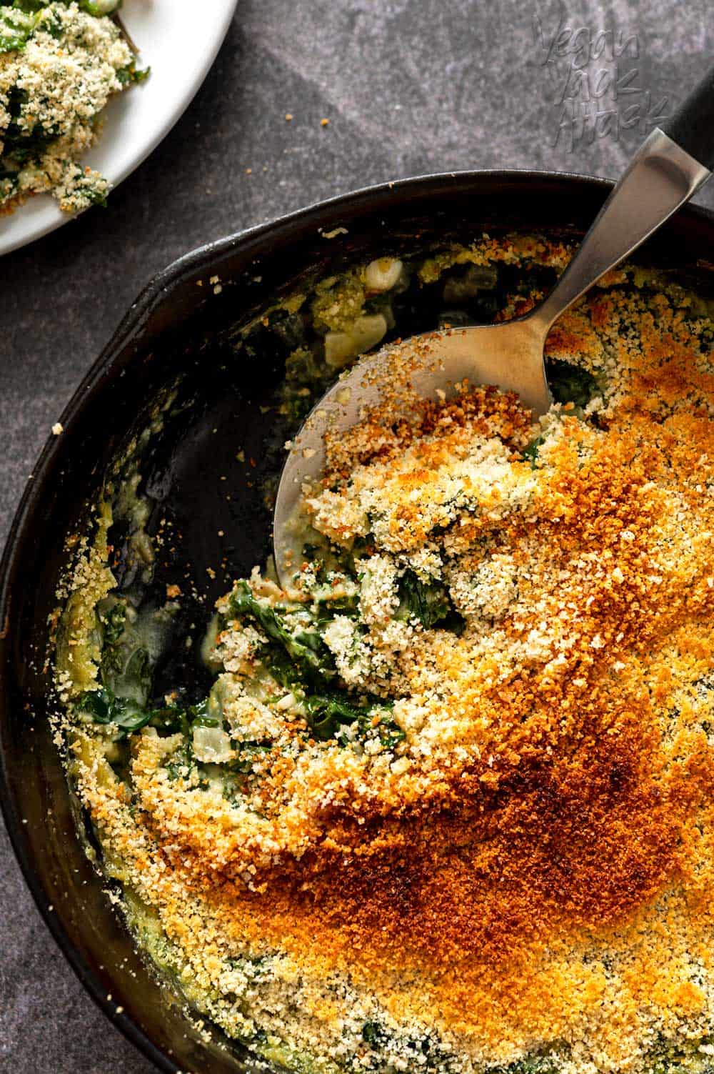 Serving spoon in a cast iron skillet filled with creamed kale next to dinner plates