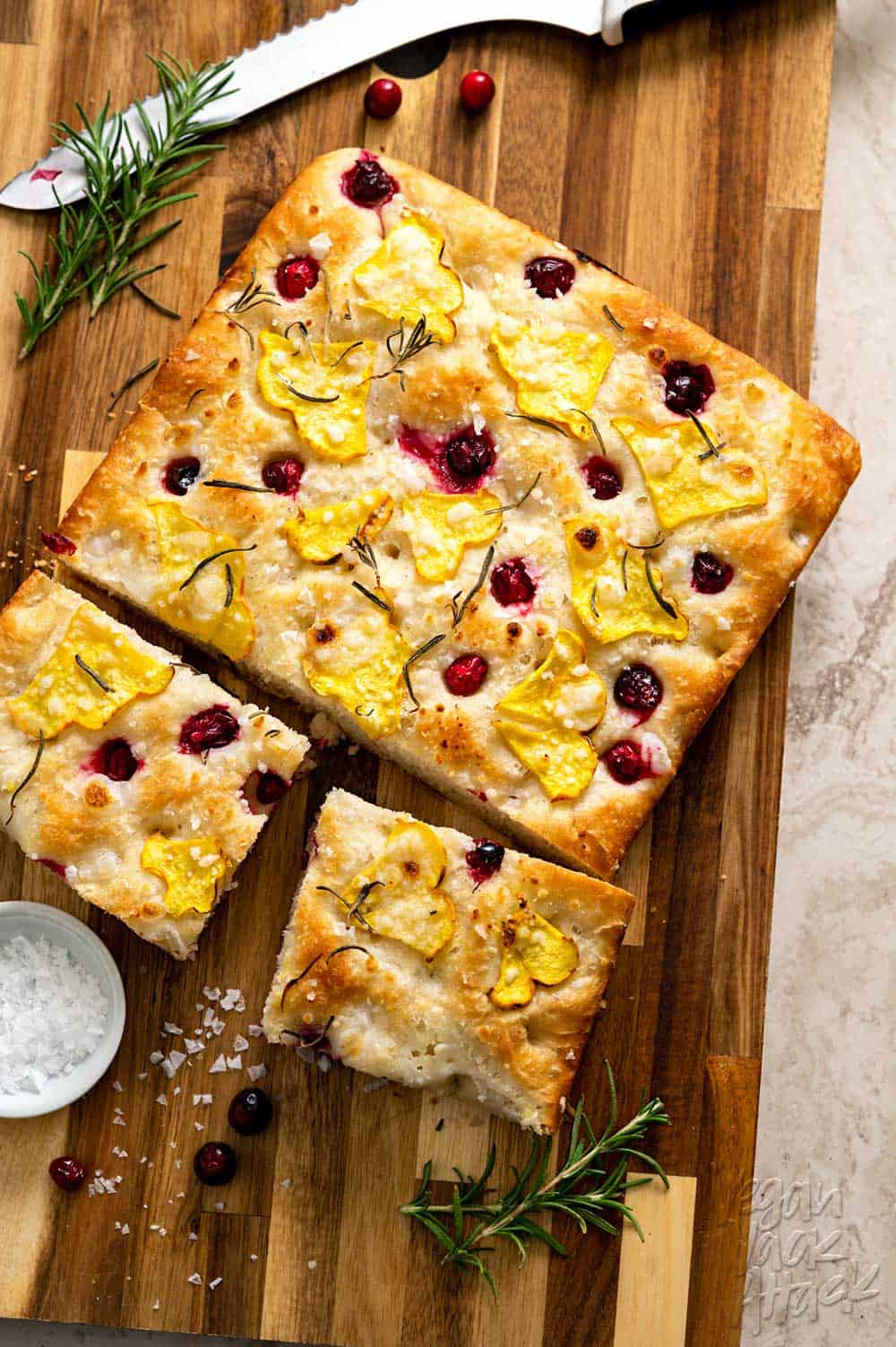Focaccia topped with squash and cranberries on a wood cutting board