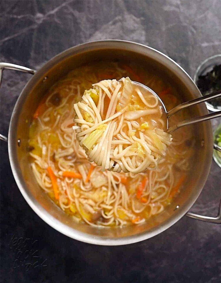 Scooping noodle soup out of a large pot with a ladle