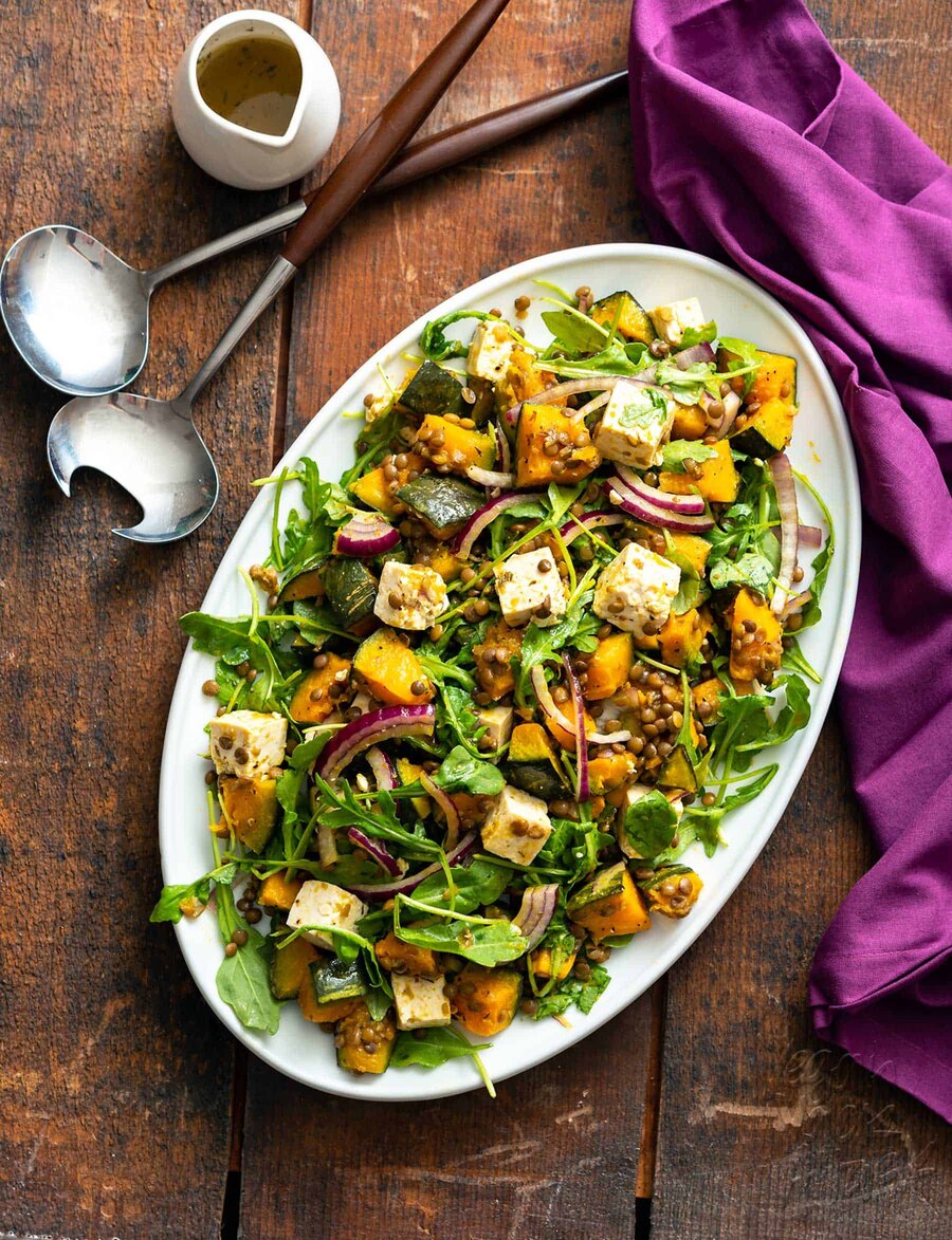 Oval plate filled with kabocha squash salad with vegan feta and lentils, on a wood table