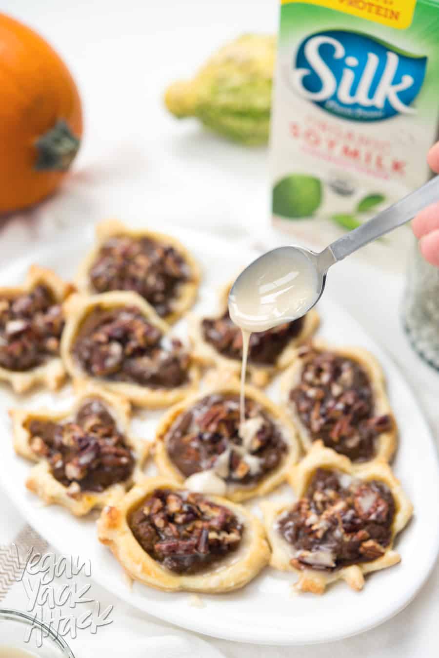 A white, oval platter filled with leaf-shaped pumpkin pastries with glaze being drizzled over them