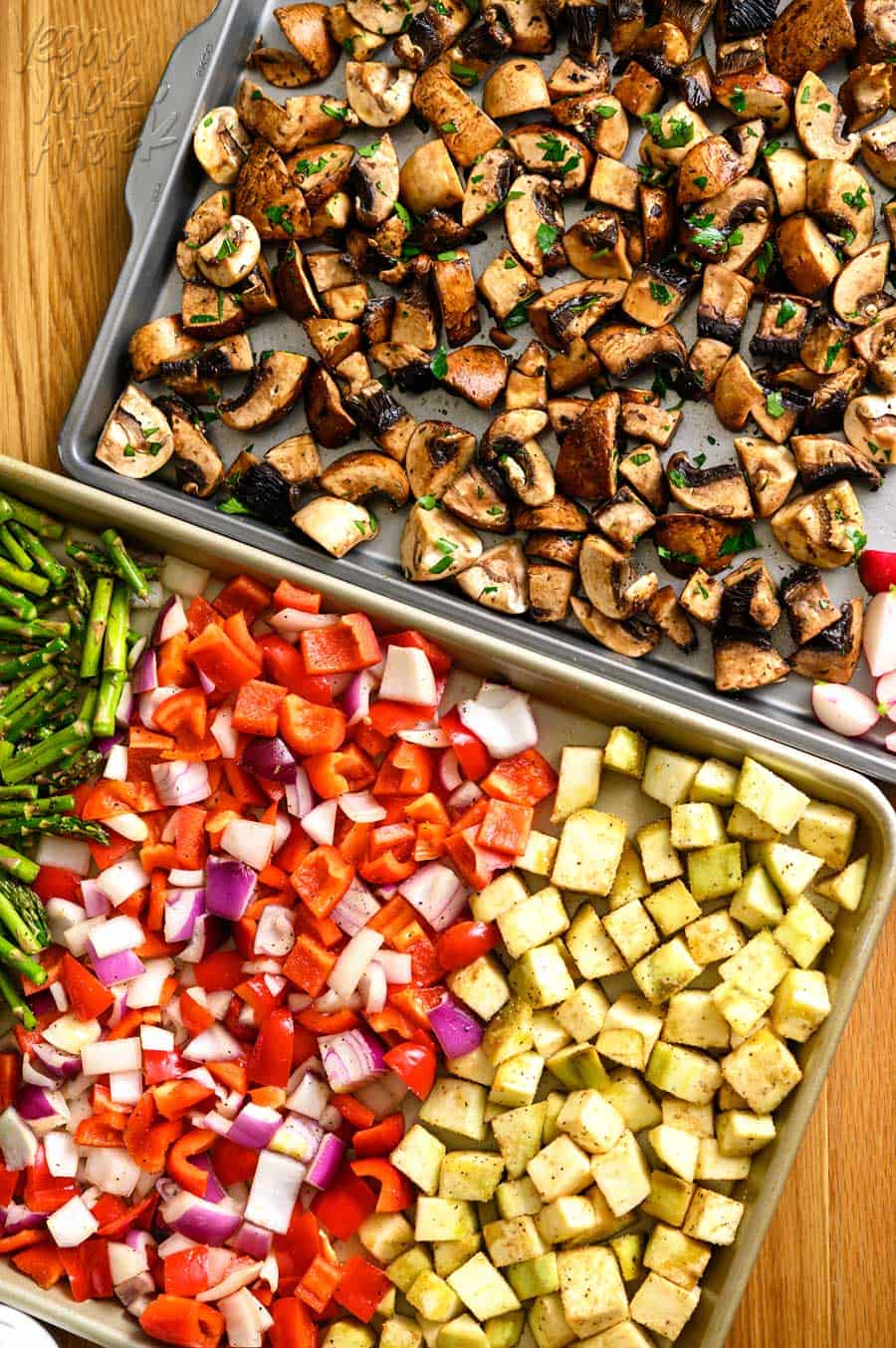 Two sheet pans with raw mushrooms and different vegetables spread across them