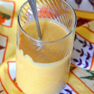 Pumpkin Protein Smoothie in a glass with spoon on a fall-themed linen