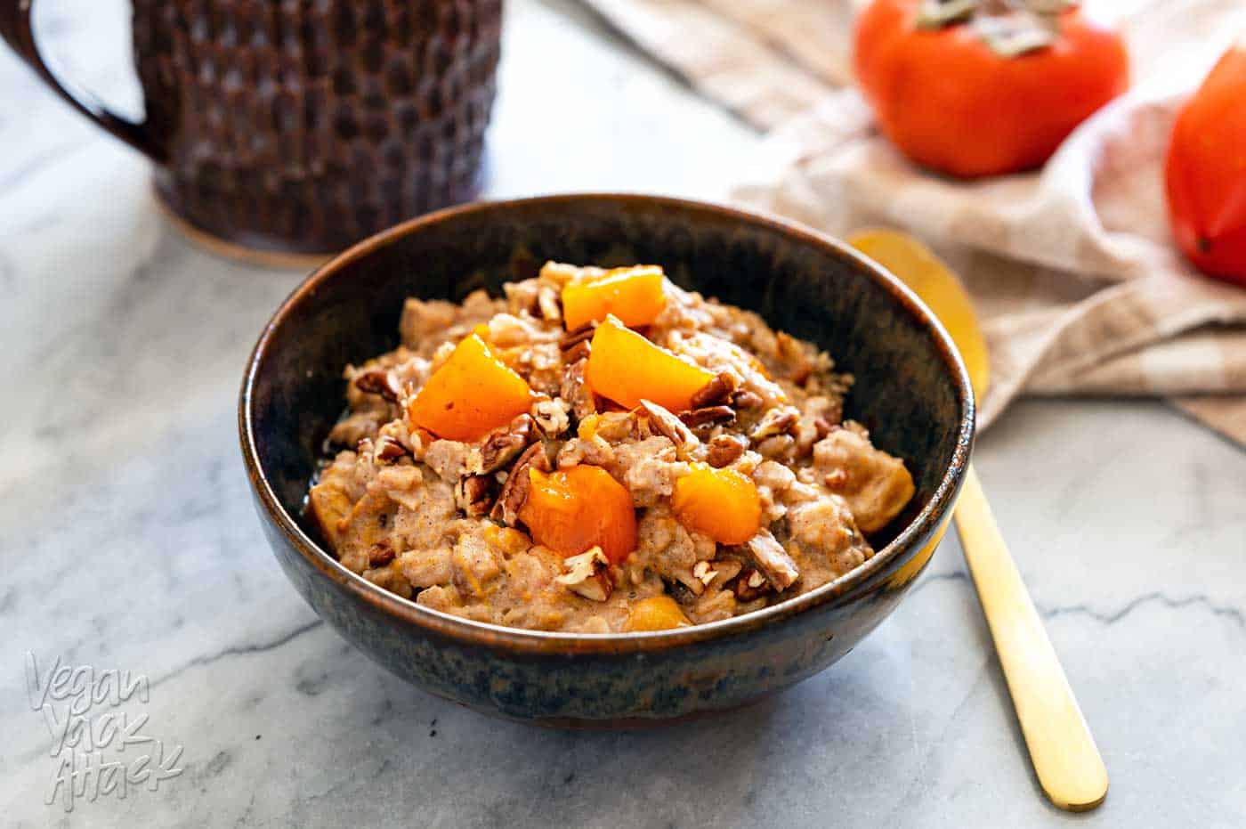 Ceramic bowl filled with persimmon oatmeal, and golden spoon, with a cup of coffee
