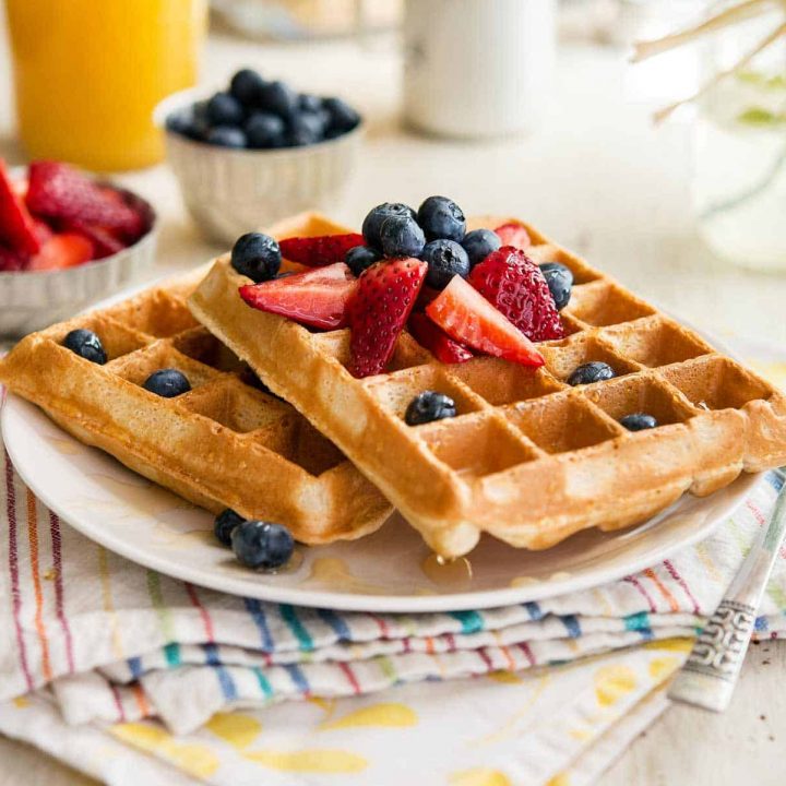 two berry pineapple belgian waffles on a white plate, topped with berries, sitting atop two colorful napkins