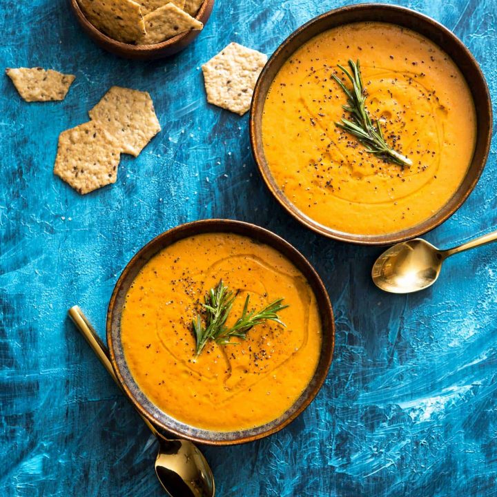 Image of two bowls of tomato bisque, with crackers on the side, on a painted blue background