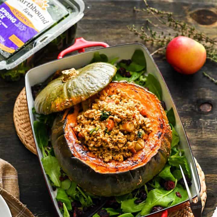 A large, roasted kabocha squash centerpiece, in a casserole dish, stuffed with a rice/tempeh mixture, on a dark background.