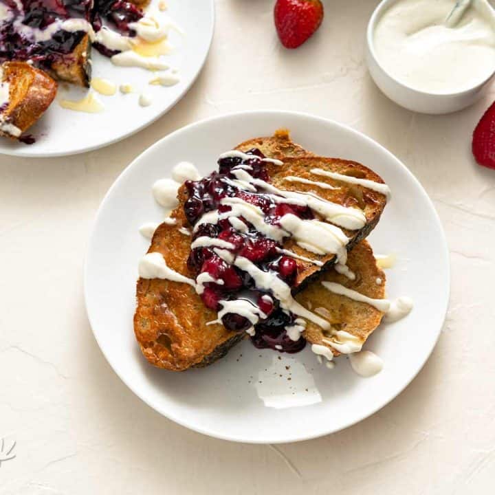 Image of two plates of berry sourdough French toast on an off-white background with cream sauce