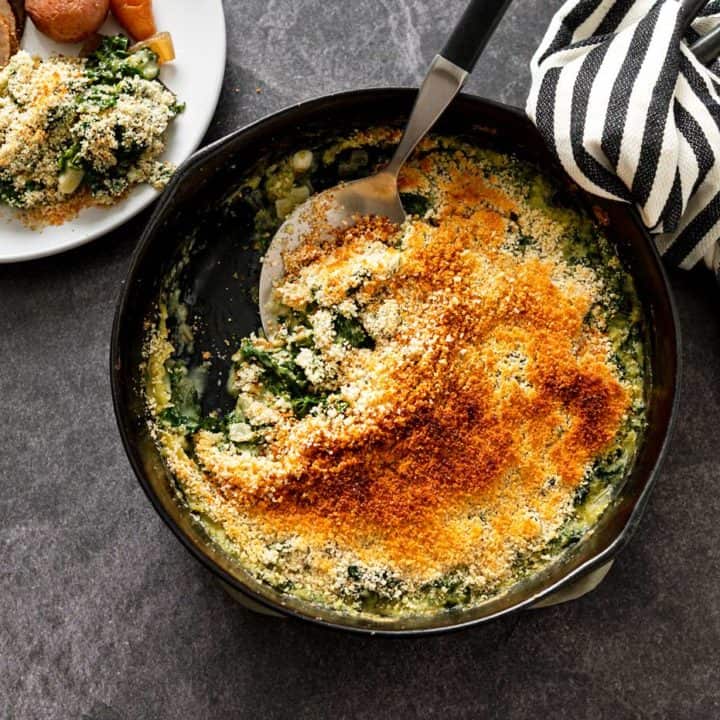 Serving spoon in a cast iron skillet filled with creamed kale next to dinner plates