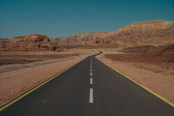 Expansive desert road under clear sky, conveying solitude and freedom.