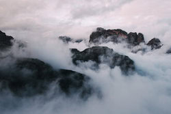 Photo art: mystical mountain peaks cutting through soft clouds.