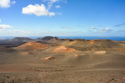 View of Timanfaya National Park with gentle volcanic landscapes and clouds in the sky.