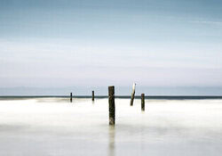 Wandbild von Manuela Deigert: ruhige Küstenaufnahme mit Holzpfählen und sanften Wellen