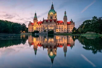 Beleuchtetes Neus Rathaus in Hannover, das sich im Wasser spiegelt.