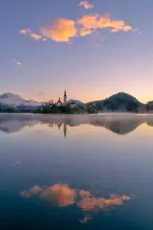 Photo art: Sunrise over Lake Bled with gentle clouds and morning mist.