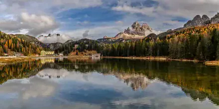 Beautiful lake in the Dolomites, surrounded by larch trees and fog.