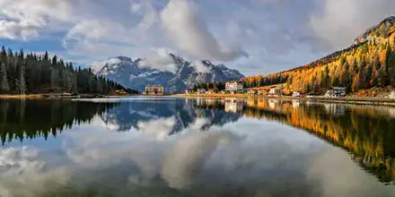 Photo art: serene view of Misurina Lake, surrounded by golden larches in autumn light.