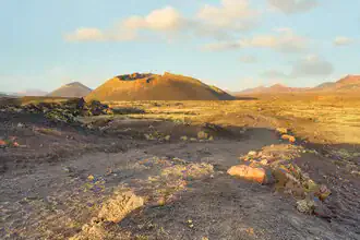 Path to El Cuervo volcano on Lanzarote with rugged terrain and soft clouds