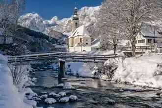 Winter scene in the Bavarian Alps featuring snow-covered mountains and a calm river